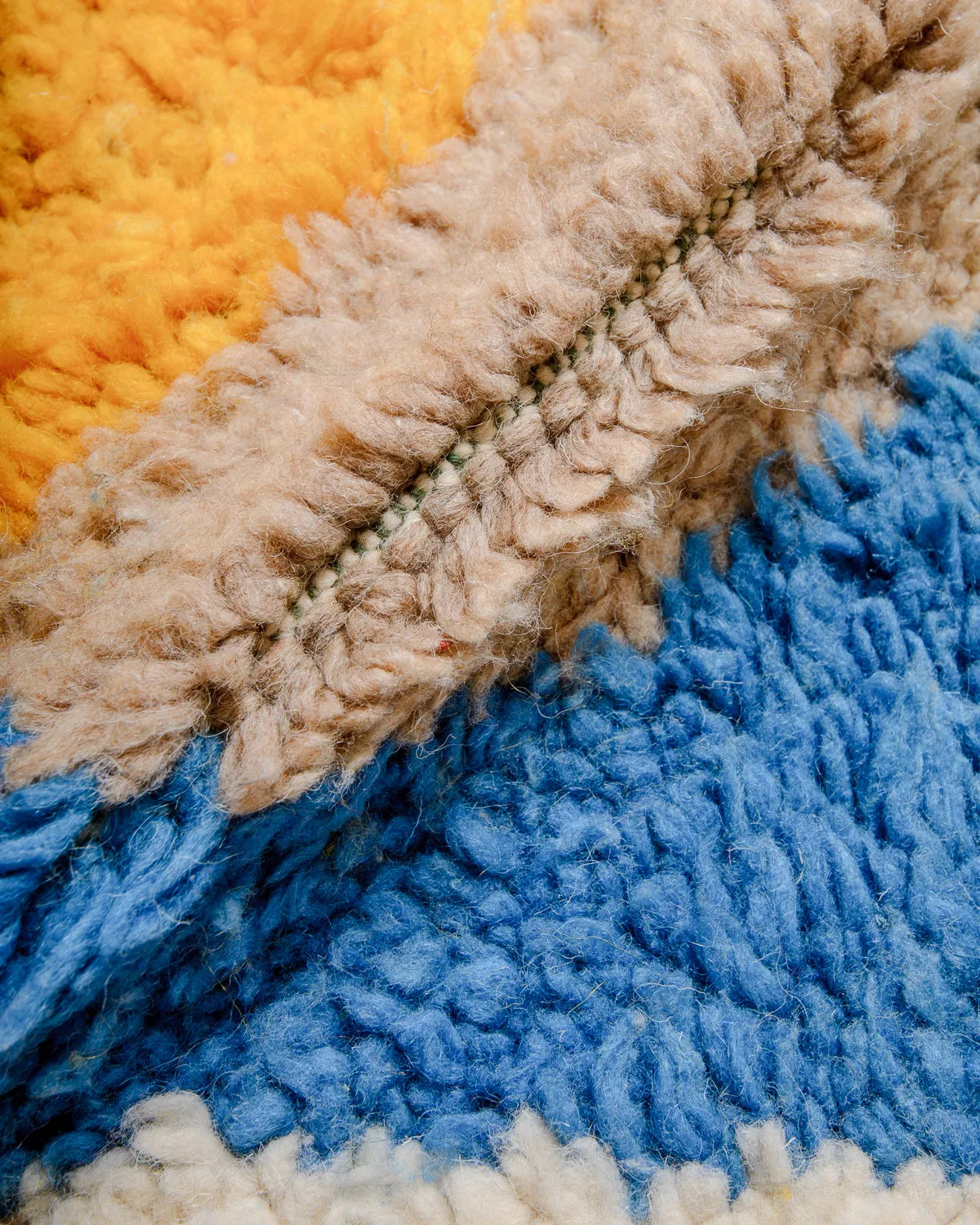 Close up of wool rug with thick pile in sand, blue and saffron yellow.